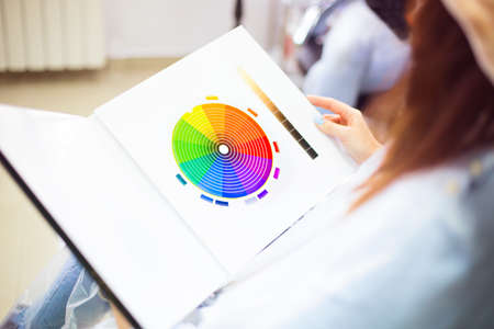 Close up of a female client examining hair color chart at the hairdressing studio coloring dyeing...