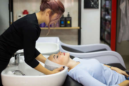 Gorgeous young woman smiling while professional hairdresser wrapping her wet hair in a towel after washing preparing for a haircut at the beauty salon. Client beauty service concept.の写真素材