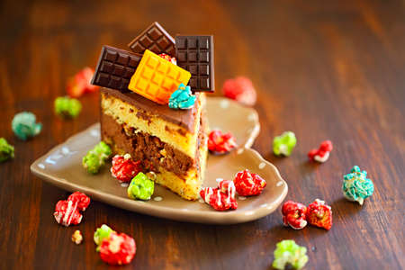 Piece of dark chocolate cake decorated with chocolate bars and pop corn on the plate, selective focus, wooden backgroundの写真素材
