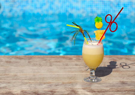 Glass of pinacolada cocktail standing on the swimming pool ledge in an tropical resort