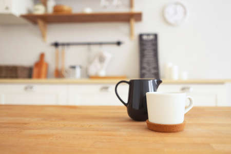 Wooden table with mug and milk jug with blurred kitchen background, copy space