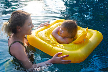 Cute little girl learning to swim with mother in pool in sunset