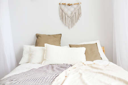 White and beige bedroom in boho style with macrame on the wall