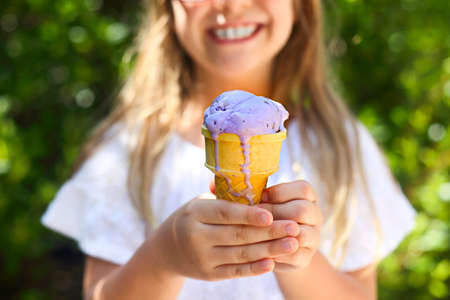 Portrait of the cute little girl with funny expression holding ice cream cone outside against bright nature background. Close upの写真素材