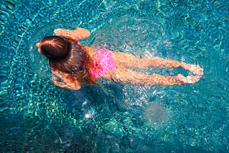 Little girl swimming in the bright outdoor pool