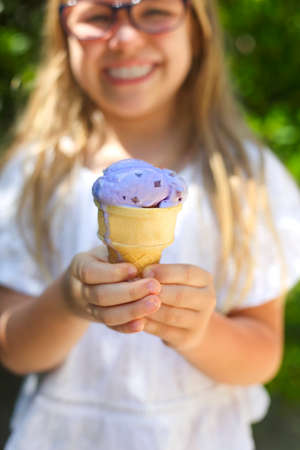 Portrait of the cute little girl with funny expression holding ice cream cone outside against bright nature backgroundの写真素材