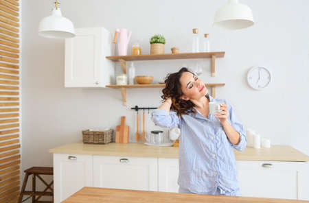 Young pretty brunette woman drinking her morning coffee at kitchenの写真素材