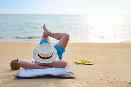 Young man in the hat with coconut cocktail on the beachの写真素材