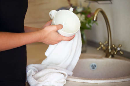 Close up of young woman drying dishes in kitchen with the towel