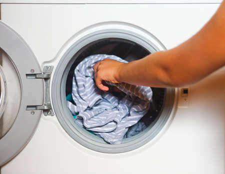 Cropped shot of young woman taking laundry from washing machineの写真素材