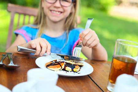 Little happy kid sitting at table and eating pancakes in the morningの写真素材