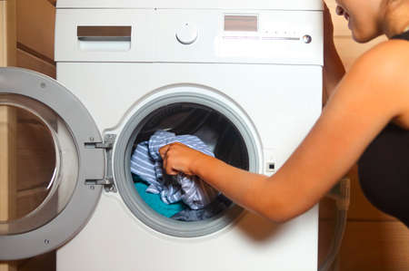 Cropped shot of young woman taking laundry from washing machine の写真素材