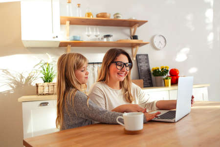 Portrait of the mother with little girl using laptop in the kitchenの写真素材
