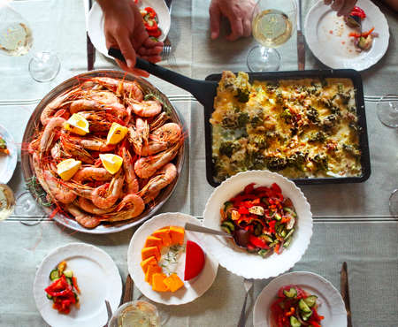 The top view on a table with food and white wine. Gratin, salad and seafood on the table