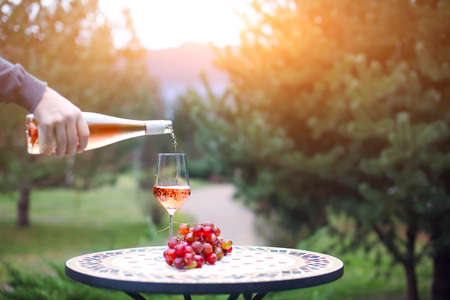 Man pouring rose wine to the glass in autumn vineyard on marble table. Harvest time, picnic or wine fest themeの写真素材