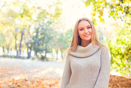 Happy blond girl posing in autumn park on yellow trees background.