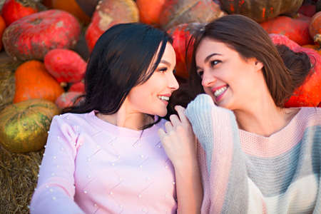 Fashionable beautiful young girlfriends together at the autumn pumpkin patch background. Having fun...