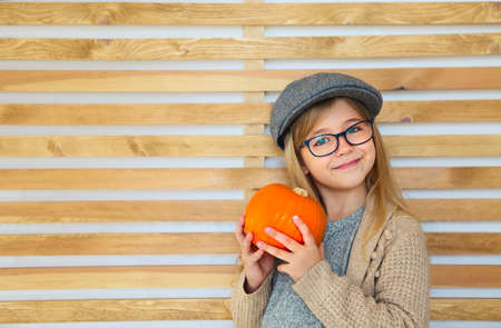 Happy little girl with autumn pumpkin by the wooden wall background. Having fun. Toned in retro style の写真素材