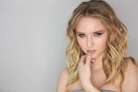 Portrait of the young beautiful woman with blonde curly hair on grey backgroundの写真素材