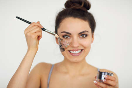 Young woman applies a magnetic dark mask on her face with a brush