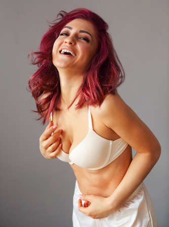 Beautiful young smiling woman with bright hair in white lingerie by the grey wallの写真素材