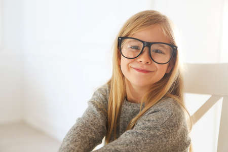 Smiling cute little girl with black eyeglasses over white background. 
Education, school, childhood, people and vision conceptの写真素材