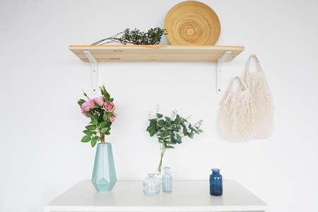 Wooden shelf and white commode with vases on it on light wall background
