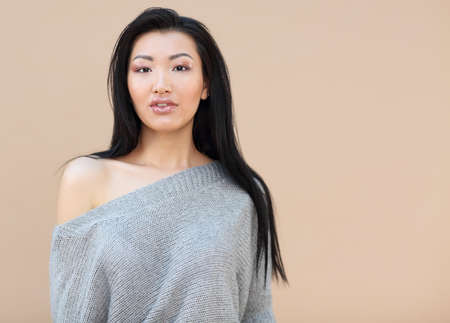 Beauty fashion portrait of sensual asian young woman with dark long hair in cozy knitted grey...
