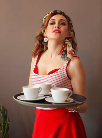 Beautiful young woman wearing bright clothes holding tray and serving coffeeの写真素材