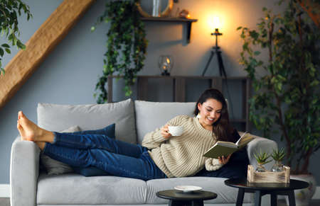 Young happy brunette woman with book wearing sweater at home