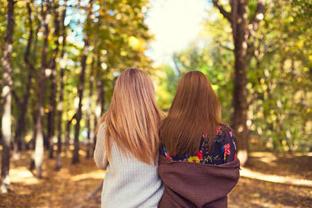 Fashionable beautiful young girlfriends walking together in the autumn park background. Having fun...