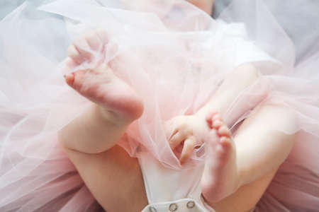 Adorable funny baby girl wearing tu-tu skirt on the bed. Close up of the feet of the babyの写真素材