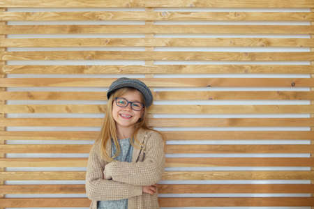 Smiling cute little girl with black eyeglasses wearing cap over wooden background. 
Education, school, childhood, people and vision conceptの写真素材