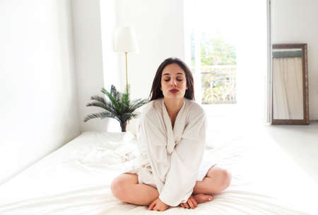 Portrait of beautiful brunette woman in white bathrobe in bedroomの写真素材