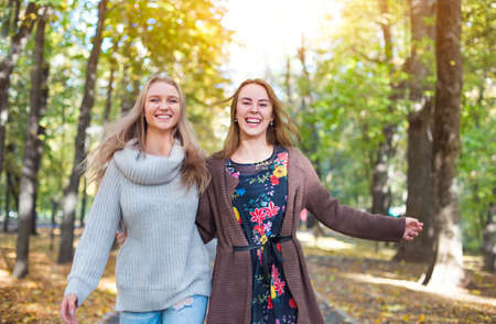 Fashionable beautiful young girlfriends walking together in the autumn park background. Having fun and posing.の写真素材