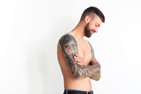Fashionable shirtless man with tattoo posing in jeans, isolated on light background
