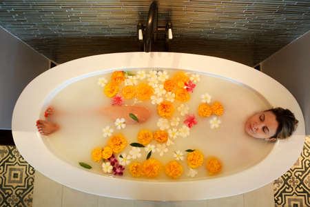 Young woman resting in bath with milk and flowersの写真素材