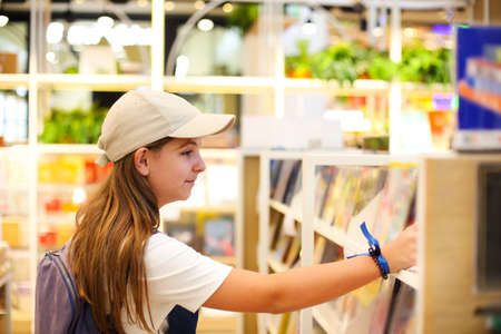 Teen girl wearing hat choosing the book in book store, education concept