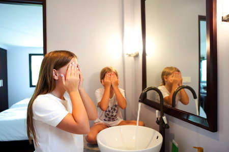 Happy children girls are washing their faces in a bathroom together