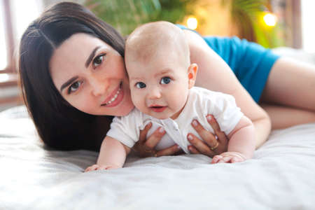 Portrait of young mother with her adorable baby boy on bed