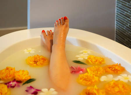 Young woman resting in bath with milk and flowersの写真素材