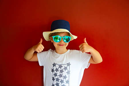 Pretty emothional child wear a hat and sunglasses on a red background. Copy space, daylight