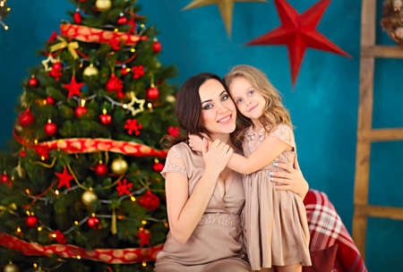 Beautiful happy mother with her ittle daughter sitting on the background of Christmas interior...