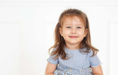 Cute little redhaired girl with blue eyes in denim jeans and blue shirt in a light roomの写真素材