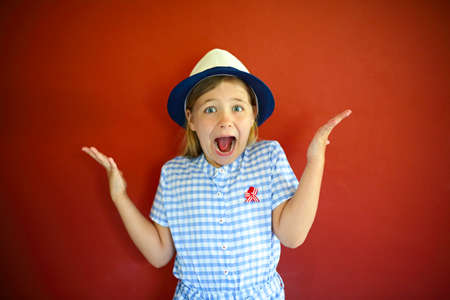 Pretty emothional children wear a hat on a red background. Copy space, daylight