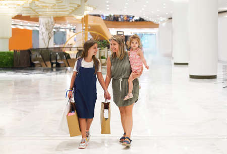 Mother and daughters walking with shopping bags on storefronts background