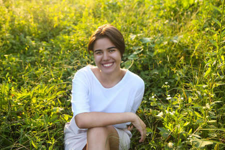 Closeup portrait of cute brunette teen girl walking at meadow field with sunlightの写真素材