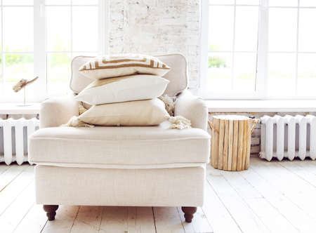 White armchair standing on the floor in front of a window shedding light on the interior of boho...
