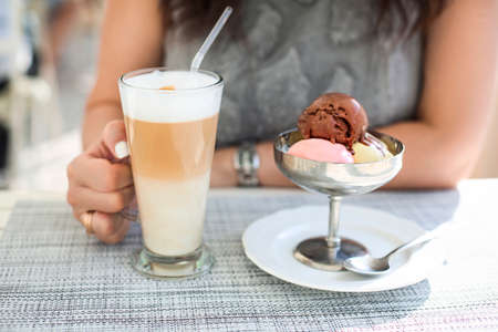 Brunette woman drinking latte coffee and eating ice cream in outdoor cafe