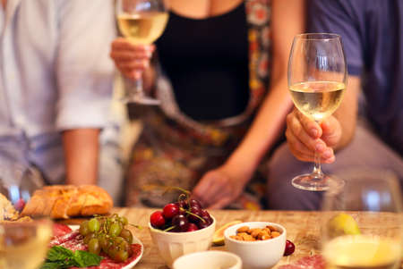 Hands of a group of people cheering with white wine and rising glasses on celebration at restaurantの写真素材